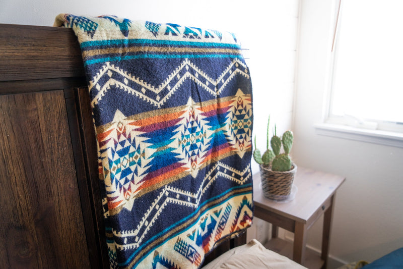 Rio Alpaca Blanket draped over a dark wooden headboard or footboard, with light shining from the side window.