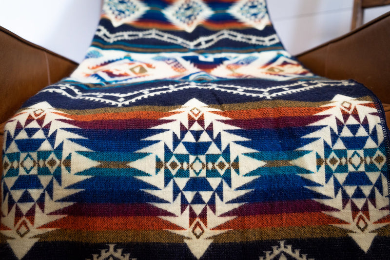 Rio Alpaca Blanket spread flat over a bed, showcasing the full, intricate, and reversible geometric design.