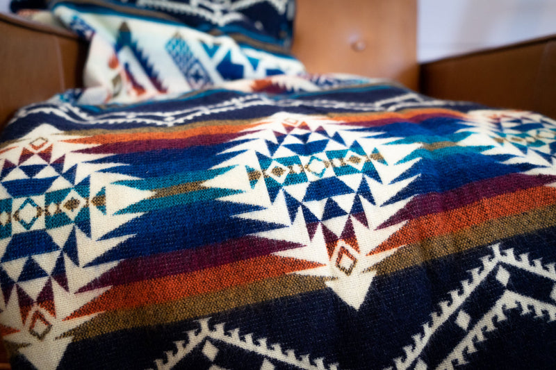 Rio Alpaca Queen Blanket draped across the foot of a bed, showing the large scale of the vibrant geometric pattern.