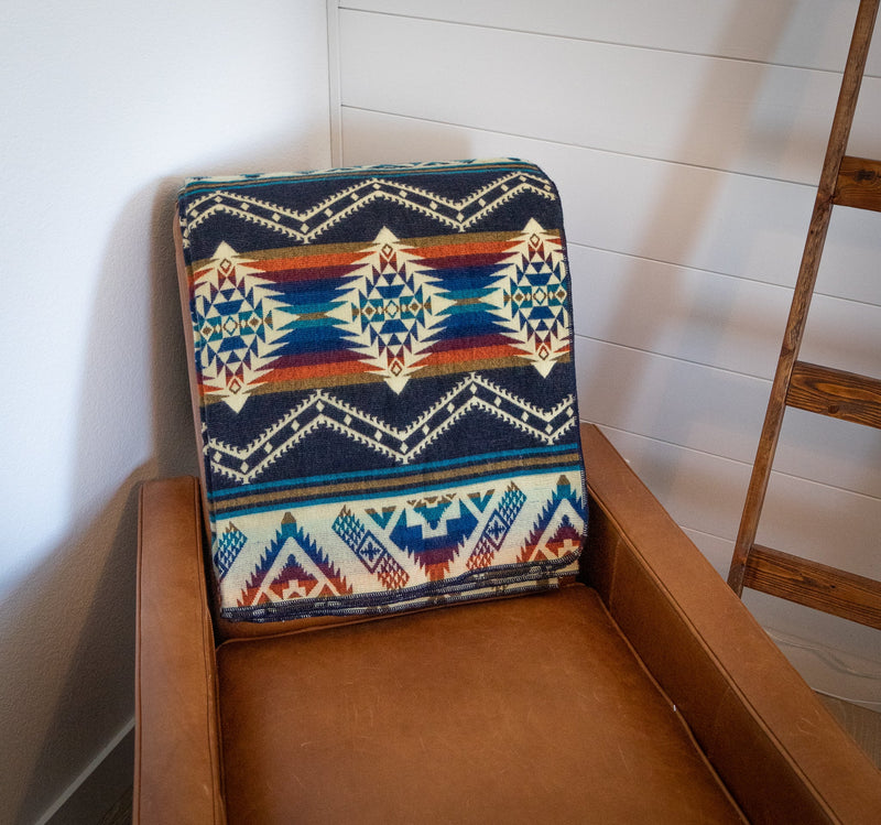 Rio Alpaca Throw folded neatly into a square and placed on a light wooden chair, emphasizing the central geometric motif.