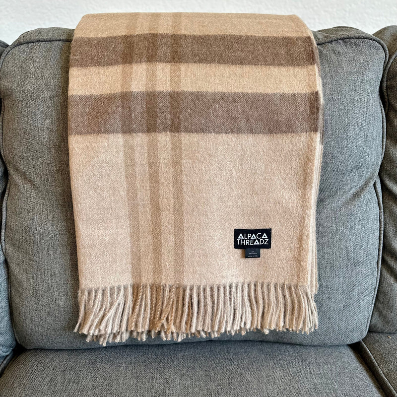Brown royal baby alpaca wool checkered throw blanket with fringe draped over grey couch – soft luxurious coastal home décor accent