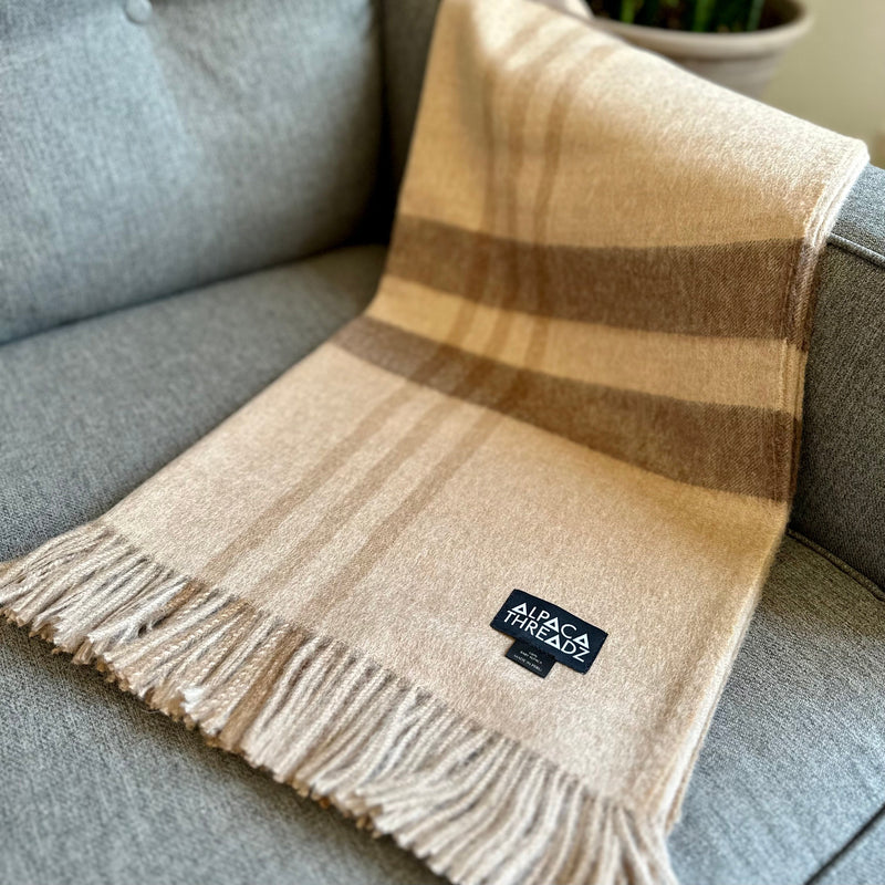 Brown royal baby alpaca wool checkered throw blanket with fringe draped over grey sofa – soft luxurious coastal home décor accent