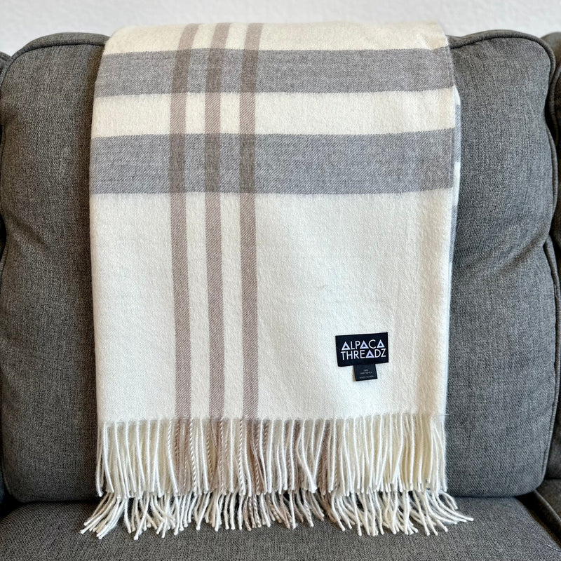 Cream royal baby alpaca wool checkered throw blanket with fringe draped over grey couch – elegant neutral coastal home décor accent