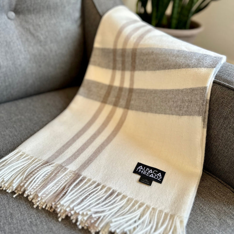 Cream royal baby alpaca wool checkered throw blanket with fringe draped over grey sofa – elegant soft coastal home décor accent