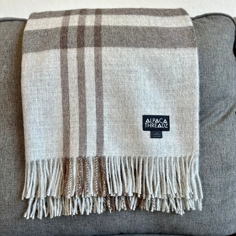 Dark grey royal baby alpaca wool checkered throw blanket with fringe draped over grey couch – premium soft coastal home décor accent