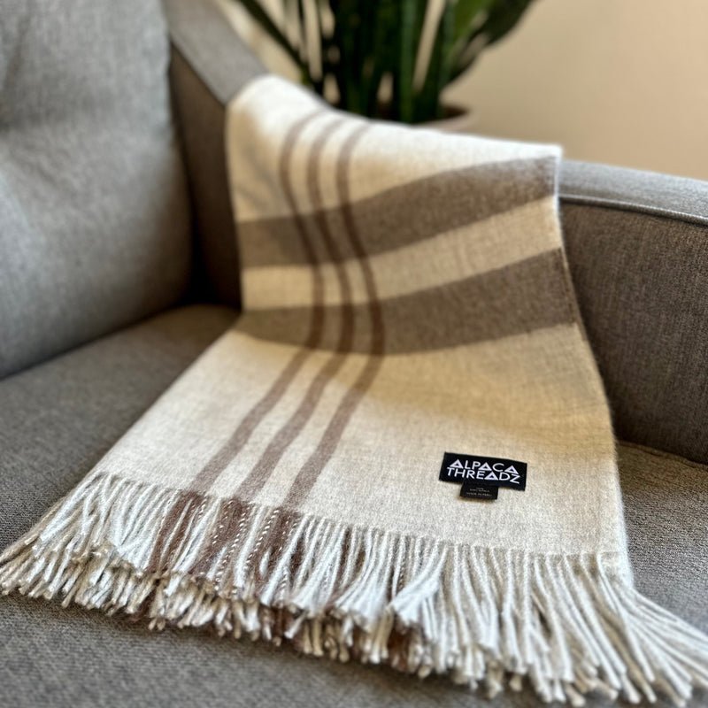 Dark grey royal baby alpaca wool checkered throw blanket with fringe draped over grey sofa – elegant soft coastal home décor accent