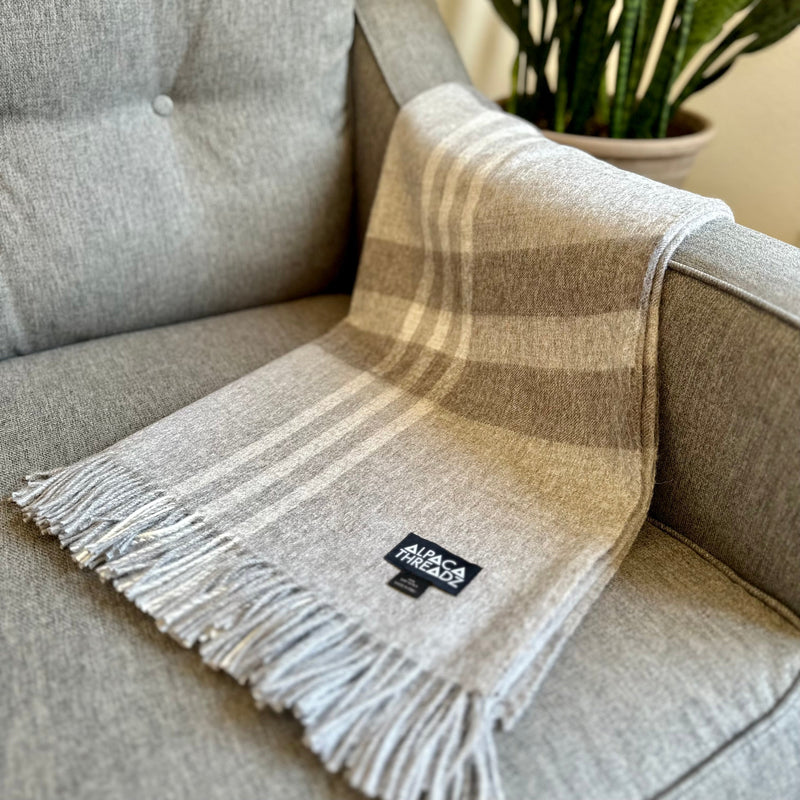 Light grey royal baby alpaca wool checkered throw blanket with fringe draped over grey chair – soft modern coastal home décor accent