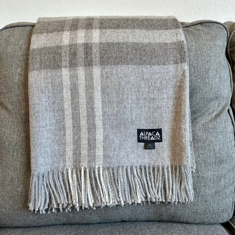 Light grey royal baby alpaca wool checkered throw blanket with fringe draped over grey couch – soft elegant coastal home décor accent