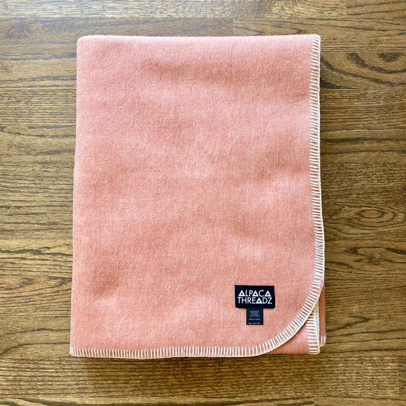 Salmon Camp Throw Blanket featuring soft woven texture in solid salmon pink, folded neatly on rustic wooden surface, cozy and lightweight design ideal for cabin or coastal décor.