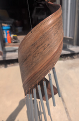 Handcrafted spiral wind chime made from natural palm frond with silver metal chimes, hanging in rustic indoor setting.