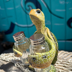 Resin sea turtle salt and pepper shaker holder with detailed shell and two glass shakers on a coastal tabletop.