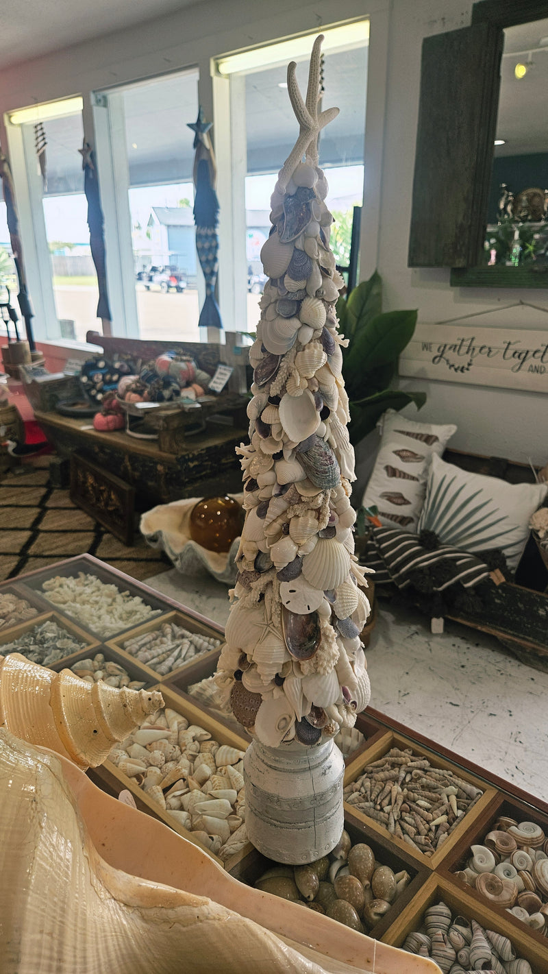Full height of the 27.5-inch seashell Christmas tree on a white base, surrounded by other coastal decor items in a brightly lit store setting.