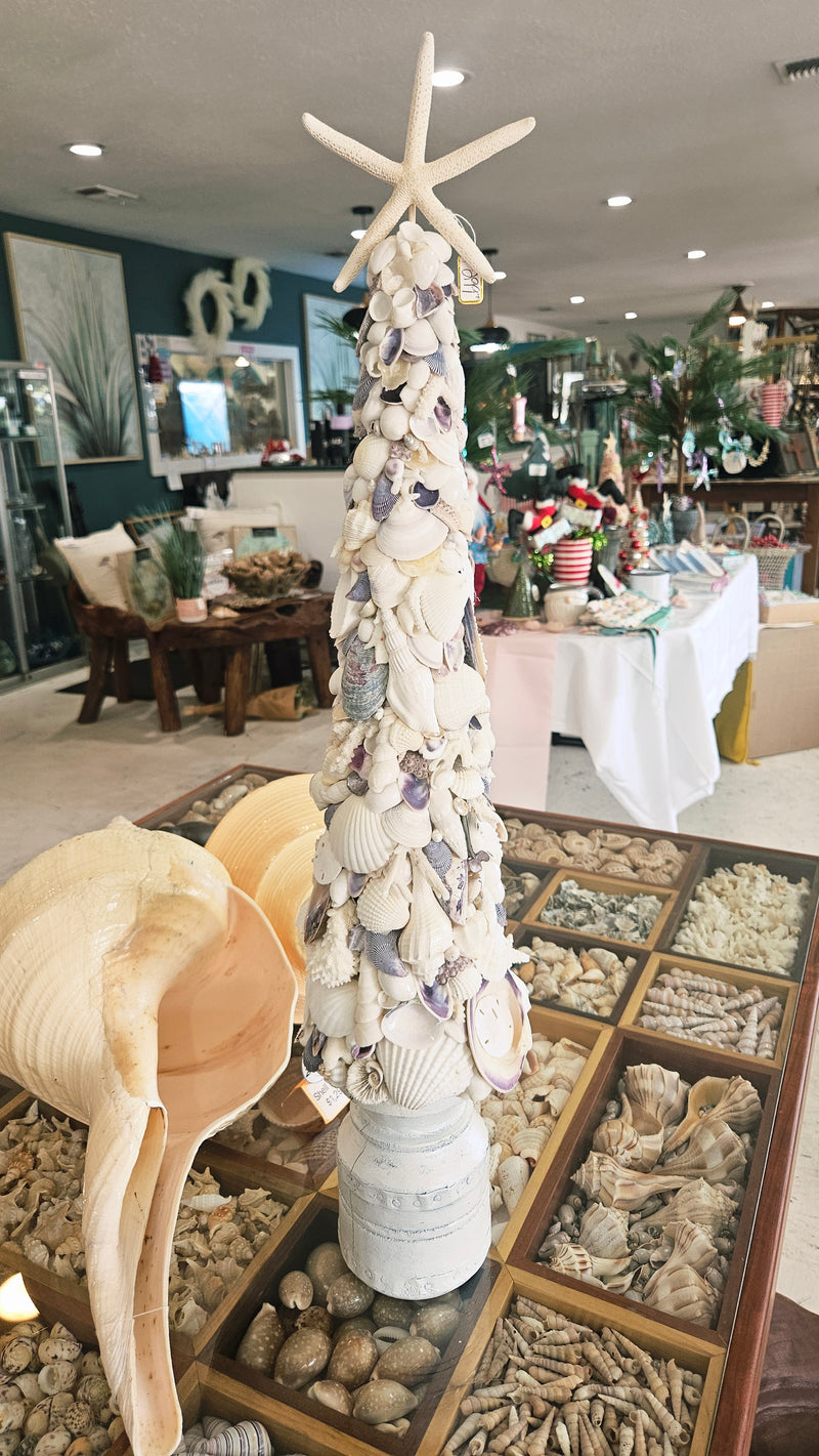 Seashell Christmas tree with a starfish topper, set atop its white pedestal base in the middle of a shop interior.