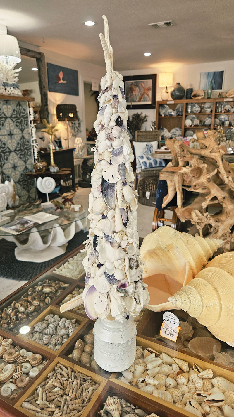 Seashell Christmas tree standing on a pedestal base as part of a wide store display featuring various shell and jewelry items.
