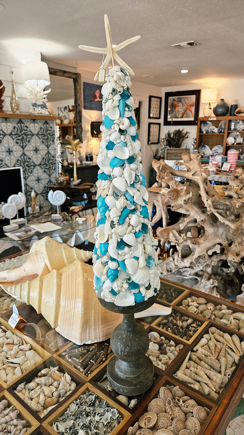 Handcrafted seashell tree standing on display in the store, showcasing the blue and white coastal aesthetic.