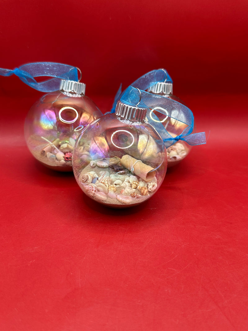 Group of three coastal glass ornaments with iridescent glow and blue ribbon, each filled with shells and sand