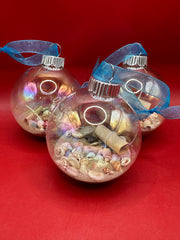 Close-up of glass Christmas ornament filled with real sand, tiny seashells, and a rolled message in a bottle tied with turquoise ribbon