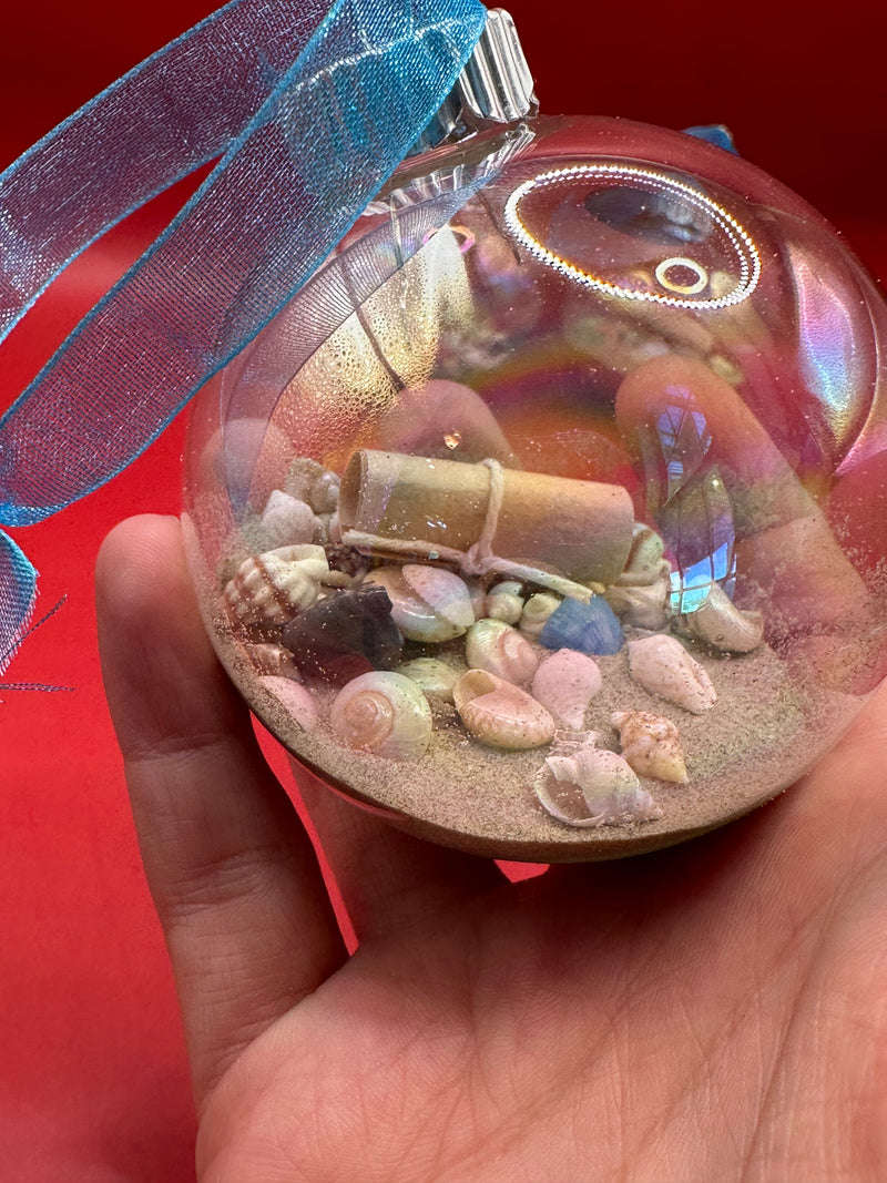 Detailed view of glass ornament featuring beach sand, colorful tiny shells, and message scroll with turquoise ribbon