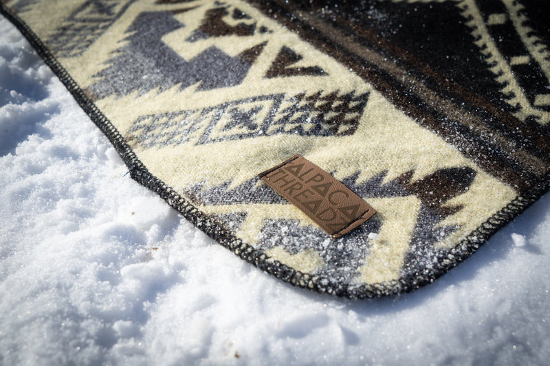 Extreme close-up of the Slate alpaca blanket pattern with the leather brand tag clearly visible on the snow-covered ground.