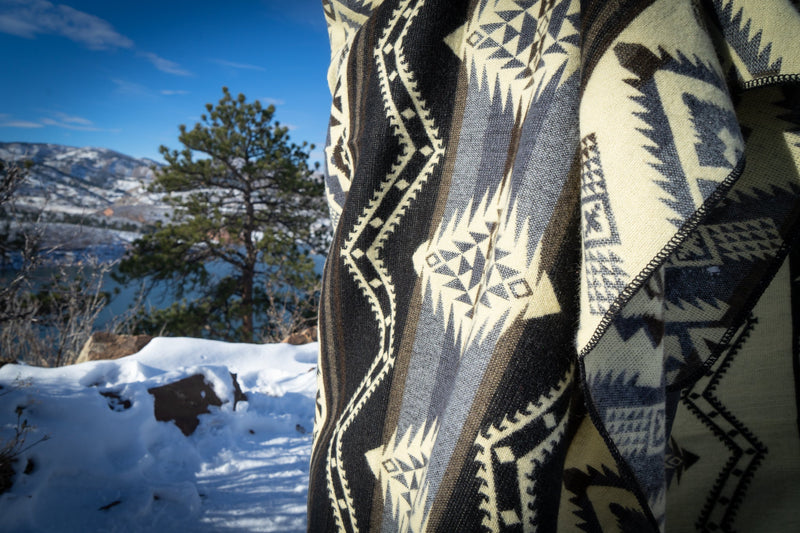 Close-up of the Slate blanket's black, gray, and cream geometric pattern against the snow, highlighting the woven texture.