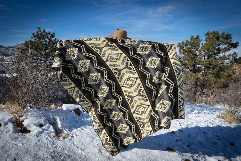 Wide shot of the Slate gray geometric alpaca blanket draped and held up, showcasing its size against a snowy mountain backdrop.