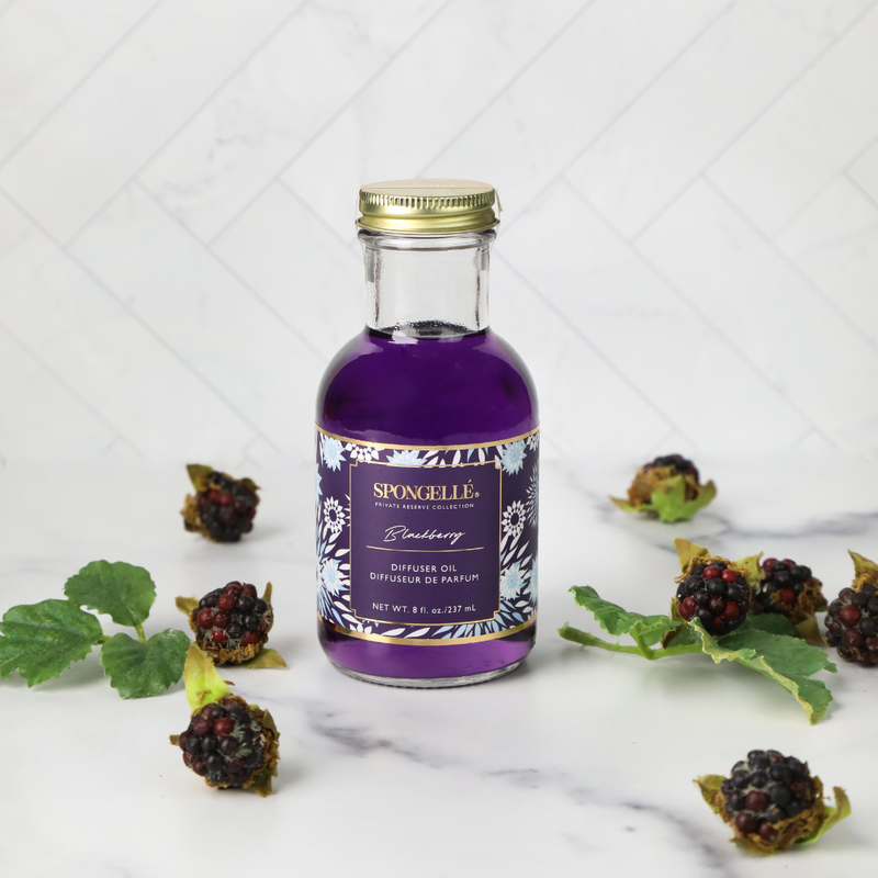 Spongellé Blackberry Diffuser Oil from the Private Reserve Collection surrounded by blackberries and greenery on white marble