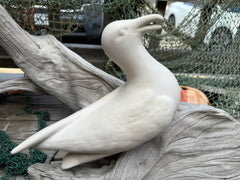 Detailed close-up of a white ceramic seagull sculpture, placed on a driftwood piece, highlighting its smooth finish and elegant design.