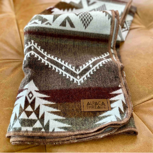 Detailed close-up of the Tan/Brown Alpaca Baby Blanket, folded to show the woven geometric pattern and fringe.