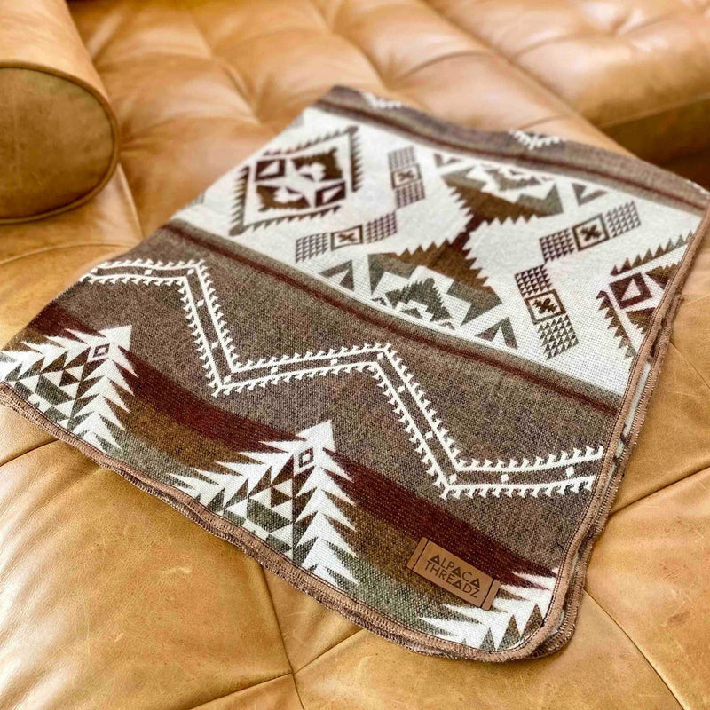 Tan/Brown Alpaca Baby Blanket draped over a brown leather armchair, emphasizing its warmth and sophisticated color palette.