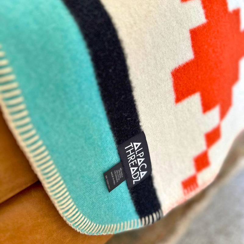 Close-up of the teal and red geometric alpaca blanket edge, showing the woven texture and a small stitched tag.
