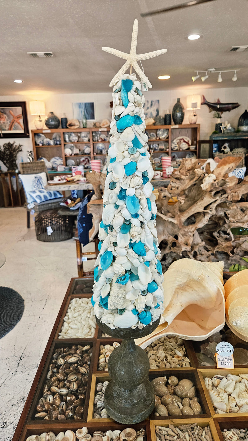 Full view of the 31.75-inch seashell tree, featuring white and turquoise shells, standing on a dark pedestal base in a coastal gift shop.