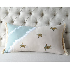 Turtle Migration Indoor Cotton Pillow featuring embroidered baby turtles, fringed edges, and coastal charm, displayed on a tufted bed.