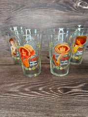 Vintage Coca Cola Magnificent Ladies Collector Series 1 Glasses featuring vibrant images of women in classic Coca-Cola advertising, displayed in a set of four on a wooden surface.