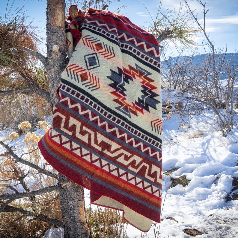 Wildfire Alpaca Blanket draped and hanging from a snowy tree branch, emphasizing the size and vibrant colors outdoors.