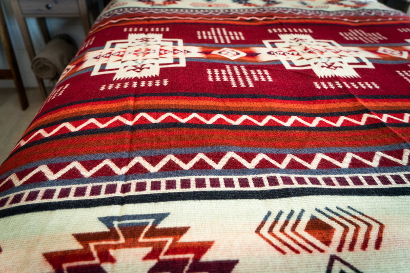 Close-up detail of the Wildfire blanket's central geometric pattern, focusing on the cream background and the dark red and blue motifs.