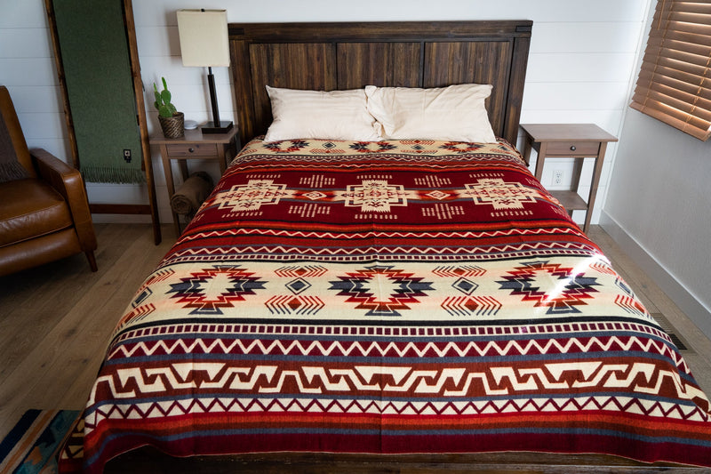Full spread of the Wildfire Alpaca Blanket covering a bed with a wooden headboard, showcasing the full Queen size geometric pattern.