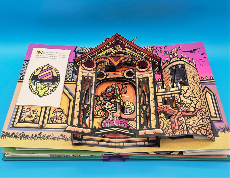 An intricate pop-up scene from the Wizard of Oz, depicting a detailed brown gate or castle entrance with the book pages opened flat.
