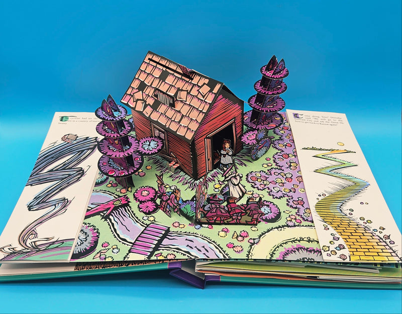 Detailed view of the Wizard of Oz pop-up book open to a scene, showing a 3D paper illustration of characters in motion.
