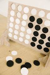 Wooden connect four game with black and white discs on a wooden floor.
