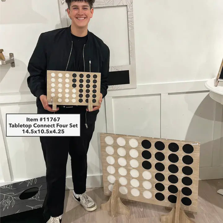 Person holding a tabletop Connect Four set in a room with white walls and a patterned rug.