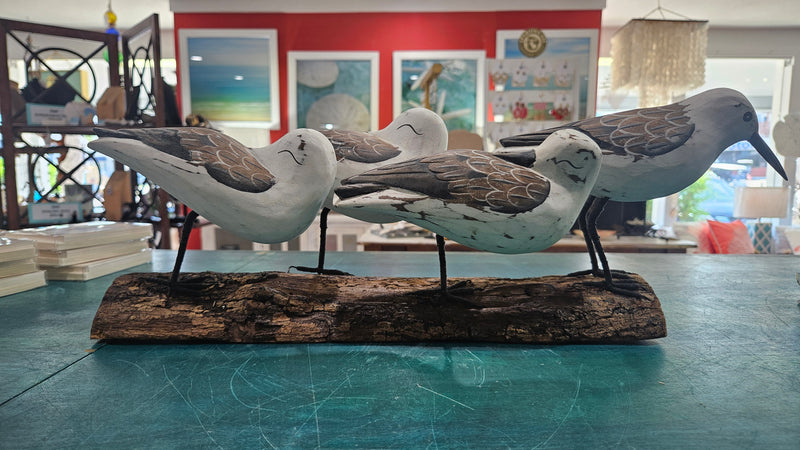 Hand-carved wooden sculpture of four coastal shorebirds on a rustic bark-style base