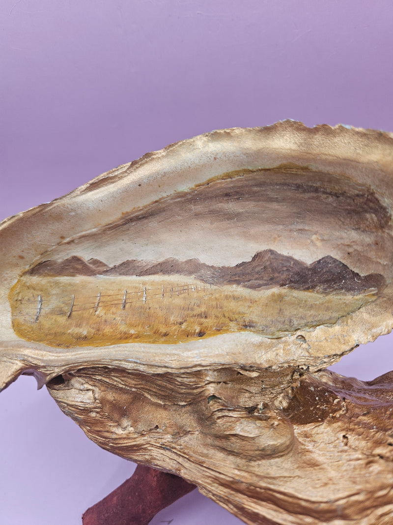 Hand-painted oyster shell resting on a wooden stand, coastal-inspired art.