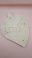 Leaf-shaped fossil marble shallow dish with subtle imprints, shown on a pale pink background.