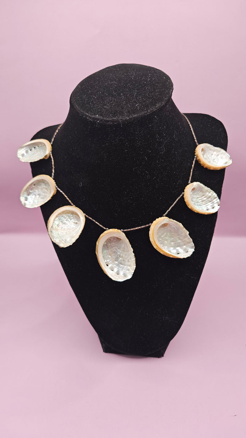 12.25" vintage abalone shell necklace with iridescent polished shells on a delicate chain, displayed on a black stand with a soft pink background.