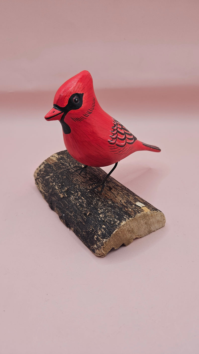 Photo of hand-carved wooden cardinal figurine, painted in bright red with black detailing, perched on a unique natural wood base.