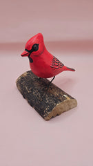 Photo of hand-carved wooden cardinal figurine, painted in bright red with black detailing, perched on a unique natural wood base.