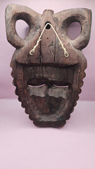 Vintage African face mask, hand-carved from wood, showcasing intricate details with natural wood grain on a pink background.