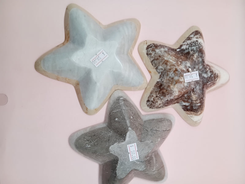 Three hand-carved onyx star bowls in brown, beige, and grey displayed vertically on a black surface