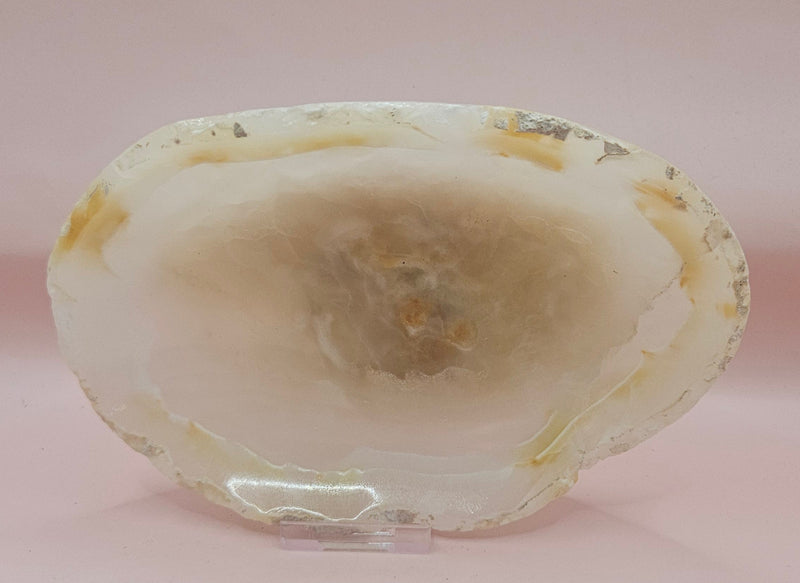 Creamy raw-edge onyx dish with soft golden veining and irregular shape on pink background