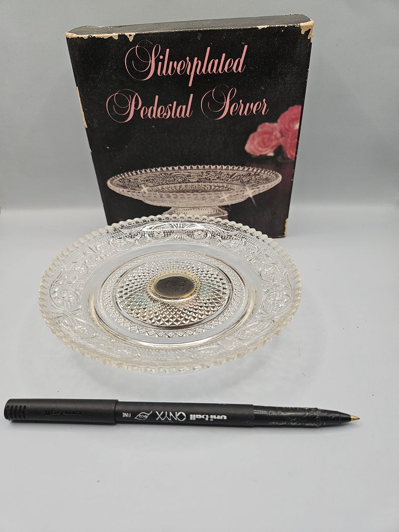 A close-up view of a silver-plated crystal pedestal server, featuring a luxurious combination of silver and crystal. The server measures 5.75"W x 1.5"H and is presented in its original packaging, perfect for serving or as a decorative item